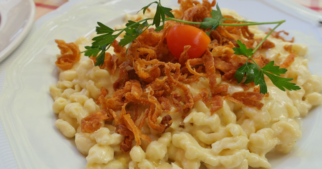 Ein weißer Teller mit Käsespätzle und Zwiebeln.